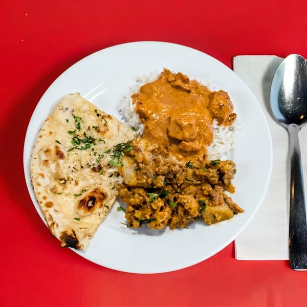 Indian meal with naan, rice, butter chicken, and another chicken dish on a white plate.
